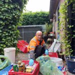Foto van Theo Lansbergen in de tuin met alle statigeld blikjes en flessen om zich heen om dit te sorteren