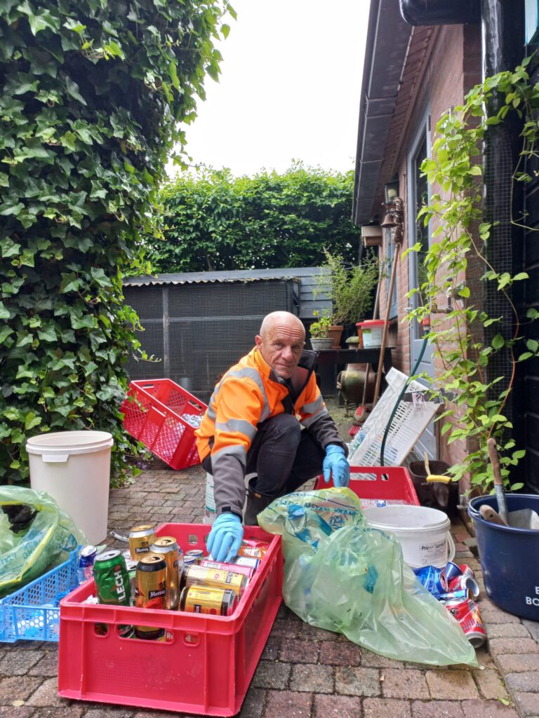 Foto van Theo Lansbergen in de tuin met alle statigeld blikjes en flessen om zich heen om dit te sorteren